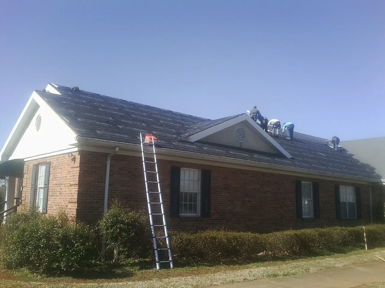 Crew tearing shingles off a brick ranch roof with a ladder set — Emergency Roof Repair work by our crew in Dupont